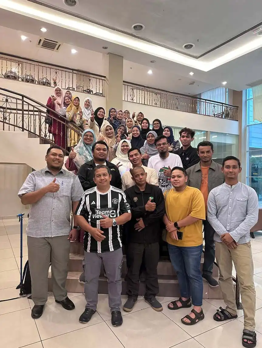 A group of people posing on a staircase indoors, some standing on steps while others are on the floor, with a backdrop of glass and trophies—a celebration of teamwork built through dedication and training. CK Media