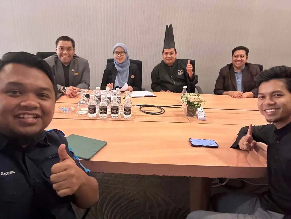 Six people sitting around a table, smiling and giving thumbs up during an enlightening training session. Bottled drinks and a small flower arrangement add charm to the scene. A chefs hat is worn by one of the individuals, injecting flair into the coaching atmosphere. CK Media