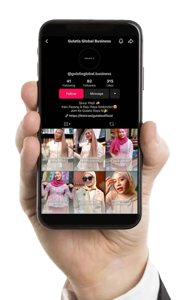 Hand holding a smartphone displaying an Instagram profile with multiple reels featuring a woman in various outfits and hijabs. The profile is named Gulatis Global Business with follow and message buttons. CK Media